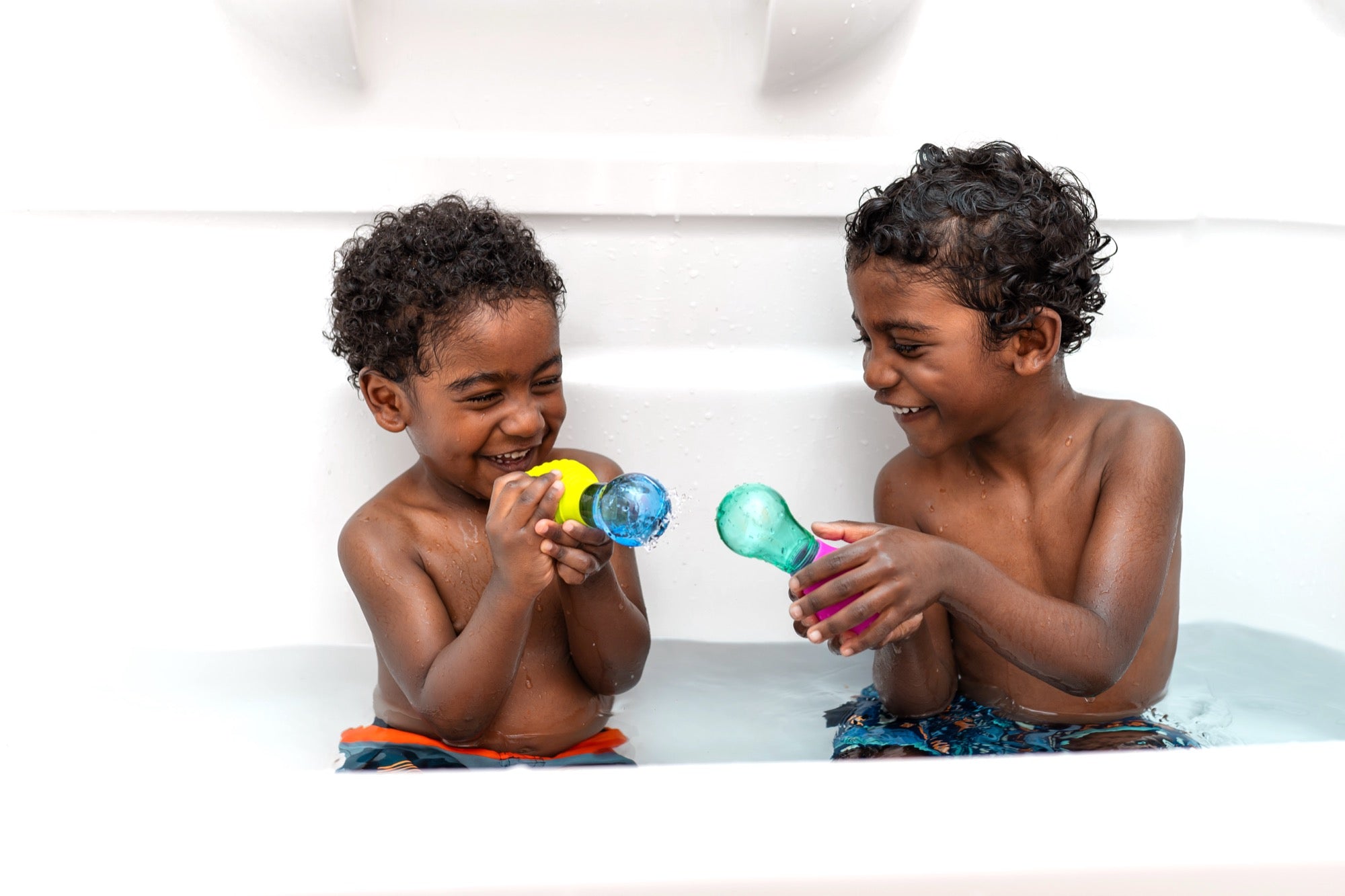 Two kids laughing in the bath playing with Möbi Skwooshlz toys